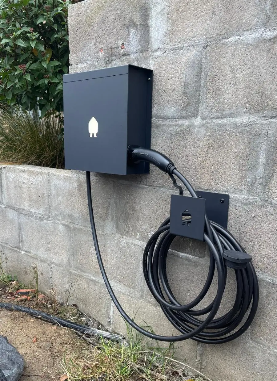 Zwarte Smappee EV Wall-laadpaal met opgerolde laadkabel, gemonteerd tegen een tuinmuur